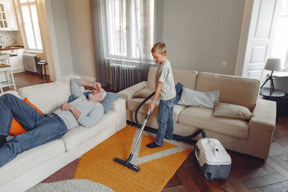 Close-up view of a carpet cleaning vacuum cleaner with a transparent dust container filled with debris and water, positioned on a pinkish-beige carpet in a domestic room. The vacuum has a black and re