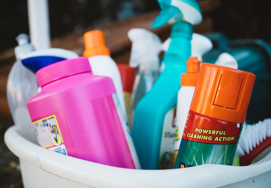Two professional cleaners from Merton Cleaner are performing surface cleaning and sanitisation in a modern kitchen. One cleaner, a woman, is vacuuming the tiled floor with a portable vacuum cleaner, e